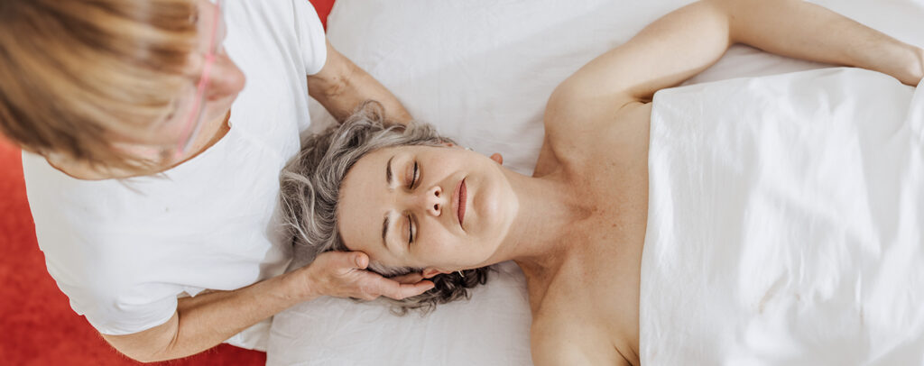 Intuitive Massage: Doris Sattelberger begleitet eine Klientin mit achtsamer Berührung im Schulter- und Nackenbereich.