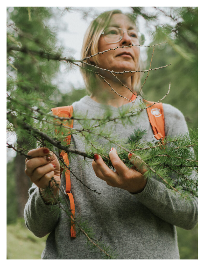 Achtsame Körperwahrnehmung in der Natur: Doris Sattelberger berührt Zweige im Wald und spürt bewusst in ihre Umgebung hinein.
